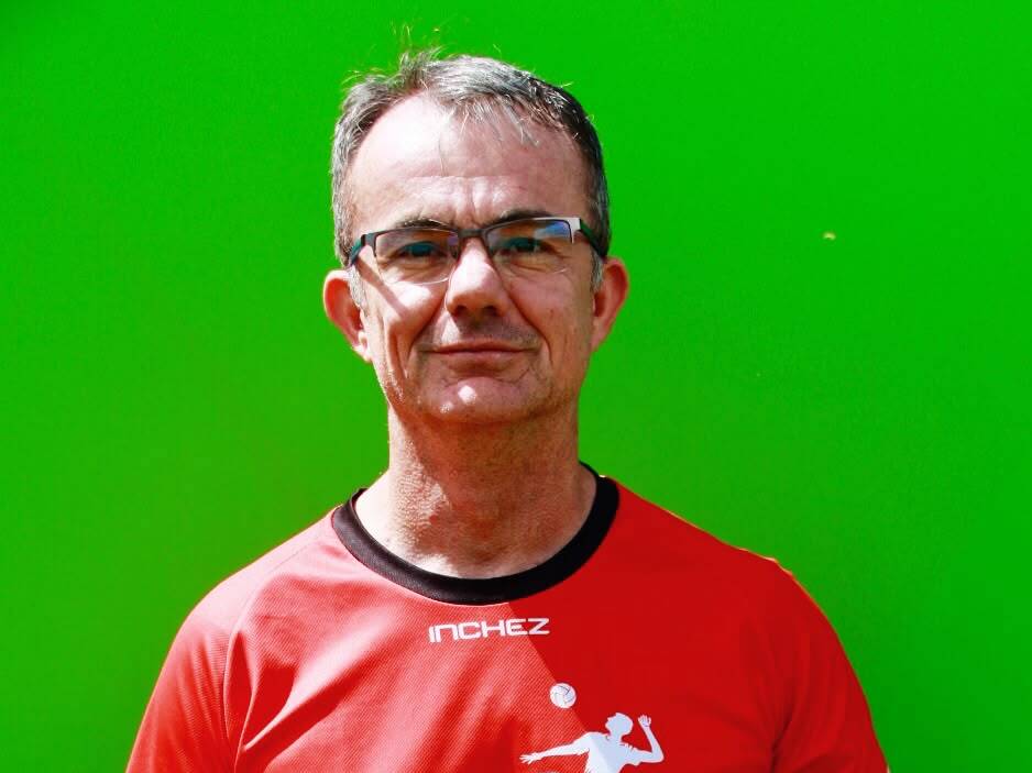 Mann in rotem T-Shirt des Potsdamer Volleyballclubs h&auml;lt einen bunten Volleyball vor einem gr&uuml;nen Hintergrund.