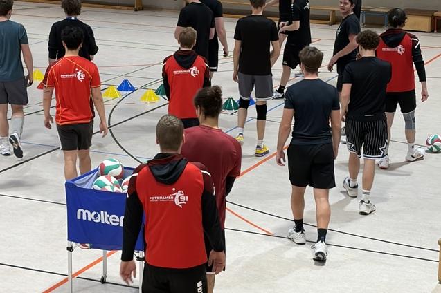 Gruppe Jugendlicher in Sportkleidung trainiert in einer Halle mit Volleyball und &Uuml;bungsmarkierungen.