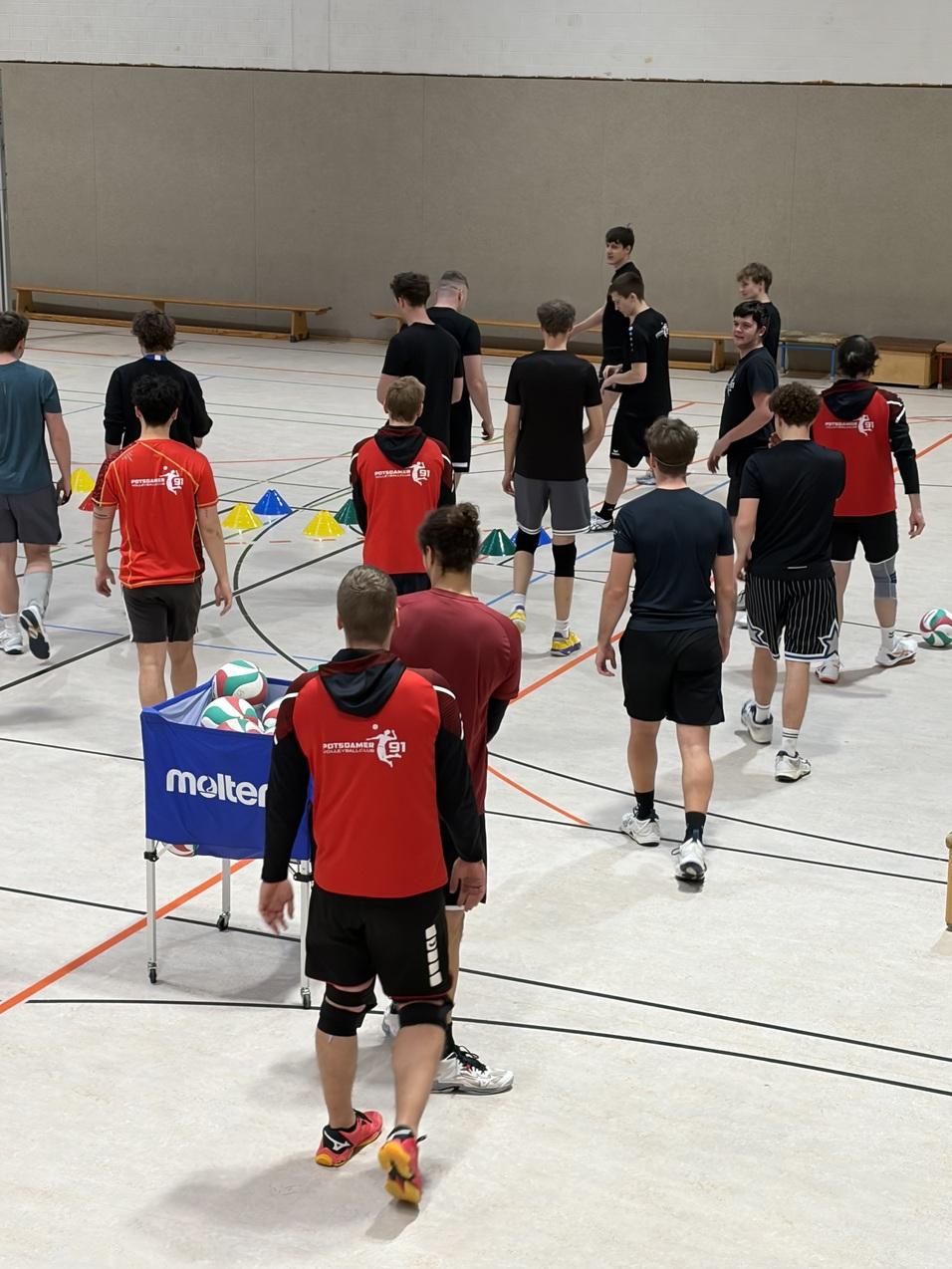 Gruppe Jugendlicher in Sportkleidung trainiert in einer Halle mit Volleyball und &Uuml;bungsmarkierungen.