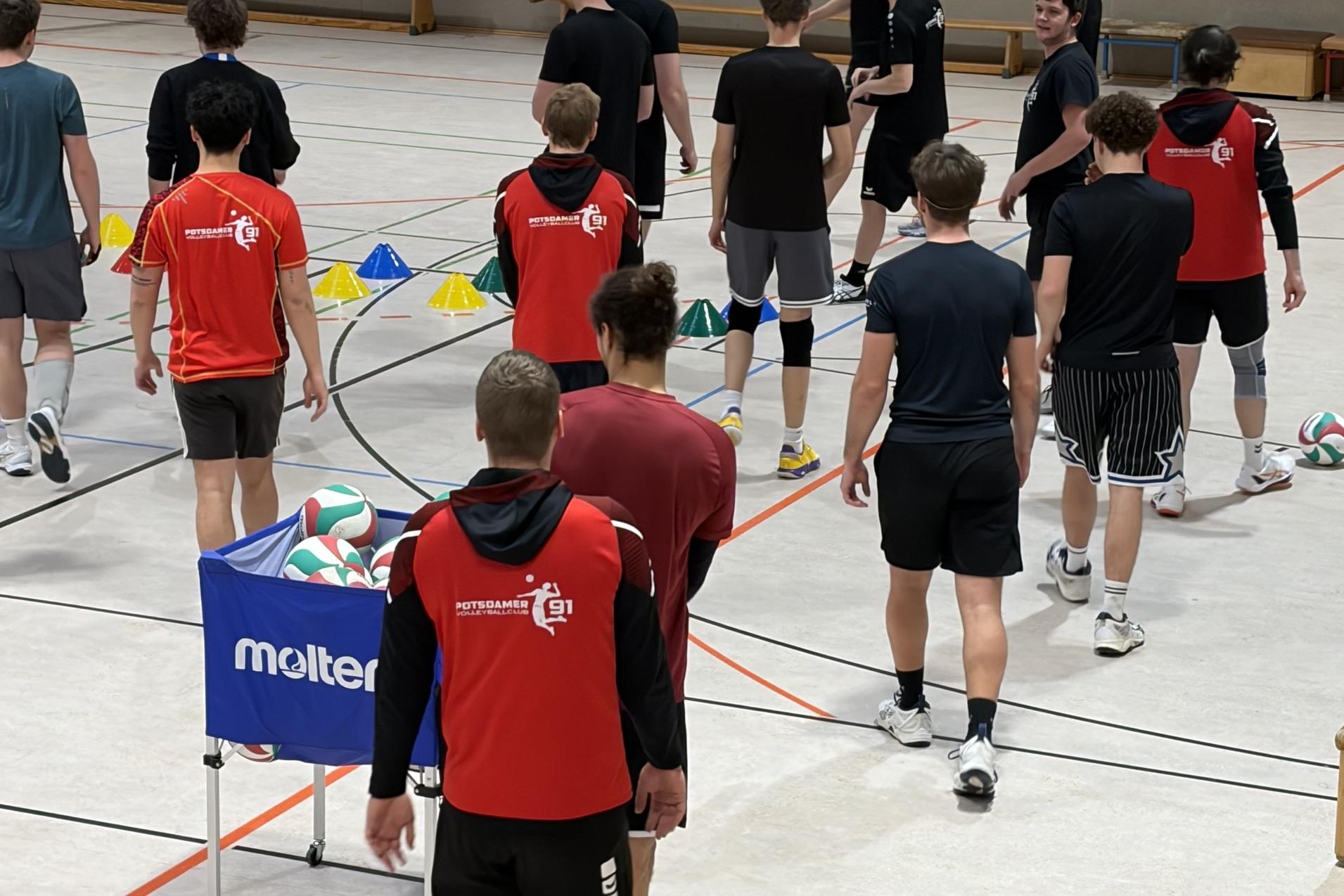 Gruppe Jugendlicher in Sportkleidung trainiert in einer Halle mit Volleyball und Übungsmarkierungen.