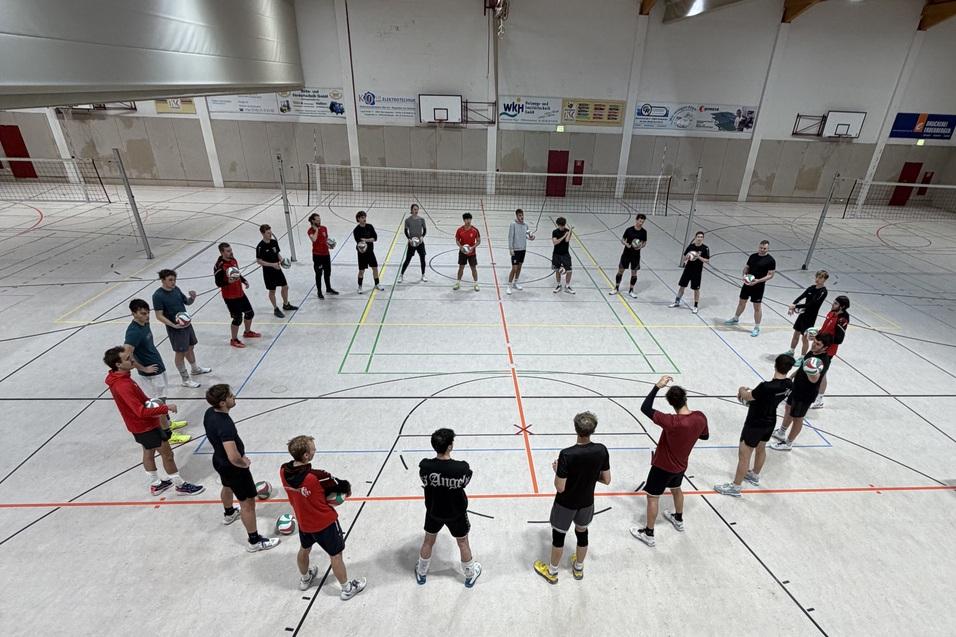 Gruppe von 20 sportlichen Jugendlichen in einem Sporthallensetting, die in einem Kreis stehen und sich auf eine &Uuml;bung vorbereiten.