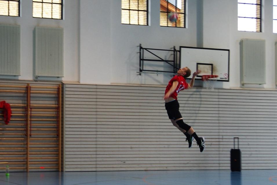 Volleyballspieler springt hoch in der Luft, bereit, den Ball zu schlagen, w&auml;hrend andere Spieler im Hintergrund stehen.