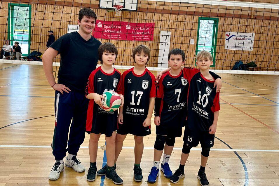Gruppennahaufnahme von vier Jungen in Sportbekleidung mit einem Volleyball, umgeben von einem Sportfeld.